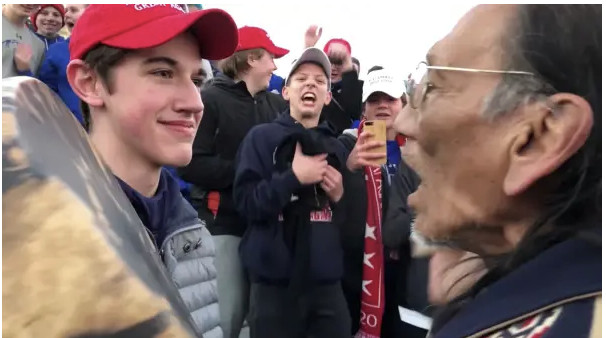 A young person in a red cap smiles beside an older man at a crowded outdoor event.